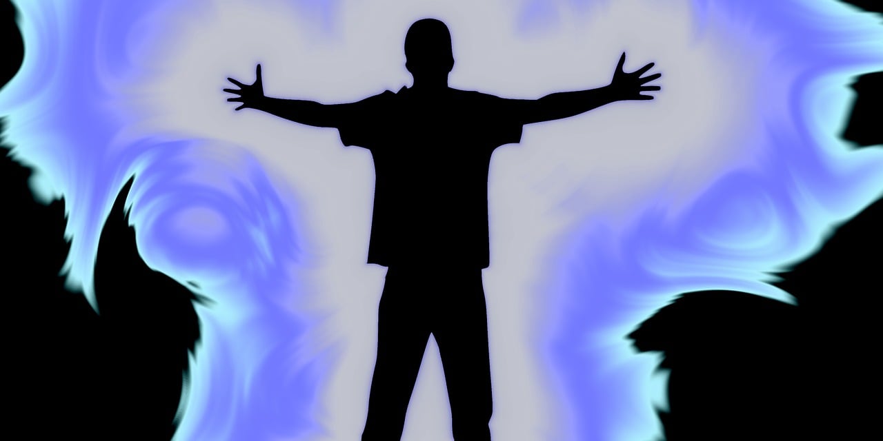 青白い炎のようなオーラの中、両腕を広げて力強く立っている男性