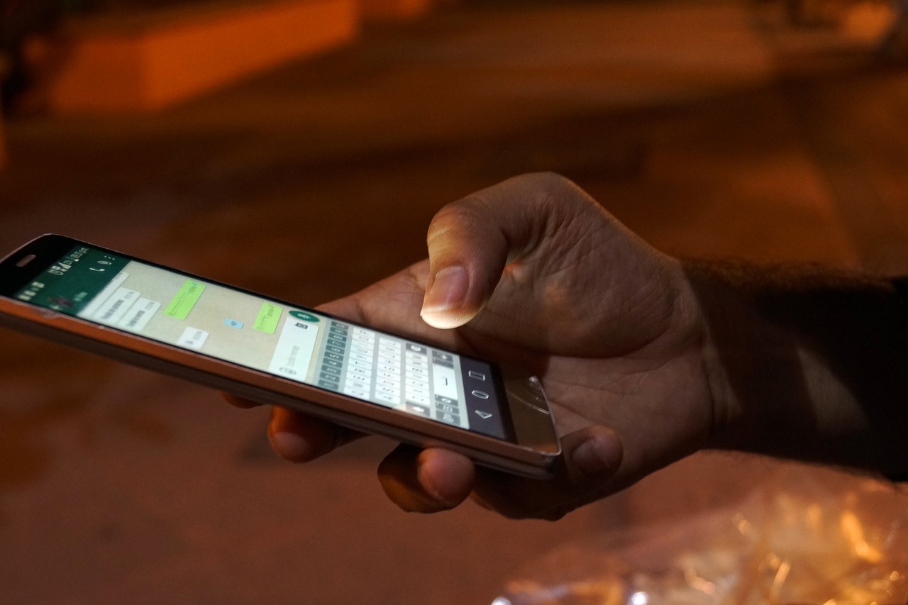 スマホで誰かとチャットしている男性の手と、薄っすらと見えるチャット画面